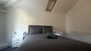 Een slaapkamer met een bed, nachtkastje, dressoir en raam.