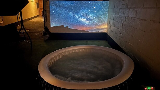 Een bubbelbad met een sterrenhemelprojectie op de muur.