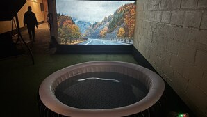 Een kamer met een bubbelbad, een projectiescherm waarop een mooi landschap te zien is, en een persoon die op de achtergrond loopt.
