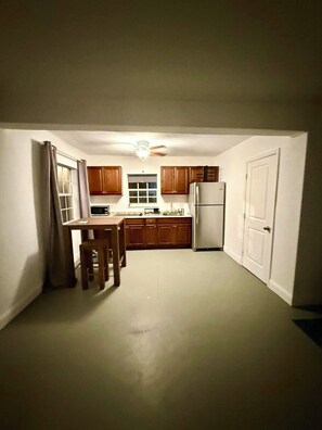 A compact kitchen with wooden cabinets, a refrigerator, and a dining table with chairs.