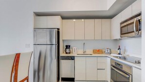 A compact kitchen with a stainless steel refrigerator, a microwave, a coffee maker, and a toaster. - Upper Sunset View - 2BR South-Facing Resort Condo (Hallandale Beach)