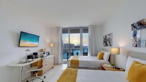 Une chambre d’hôtel avec un lit, un bureau et une vue sur le paysage urbain, grâce à de grandes fenêtres.