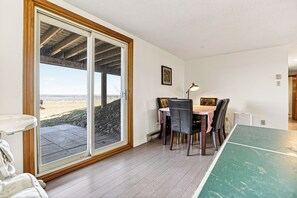 A room with a sliding glass door leading to an outdoor area, a table with chairs, a ping pong table, and a framed picture on the wall.