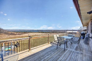 A wooden deck with a table and chairs, overlooking a landscape with a body of water and distant hills.