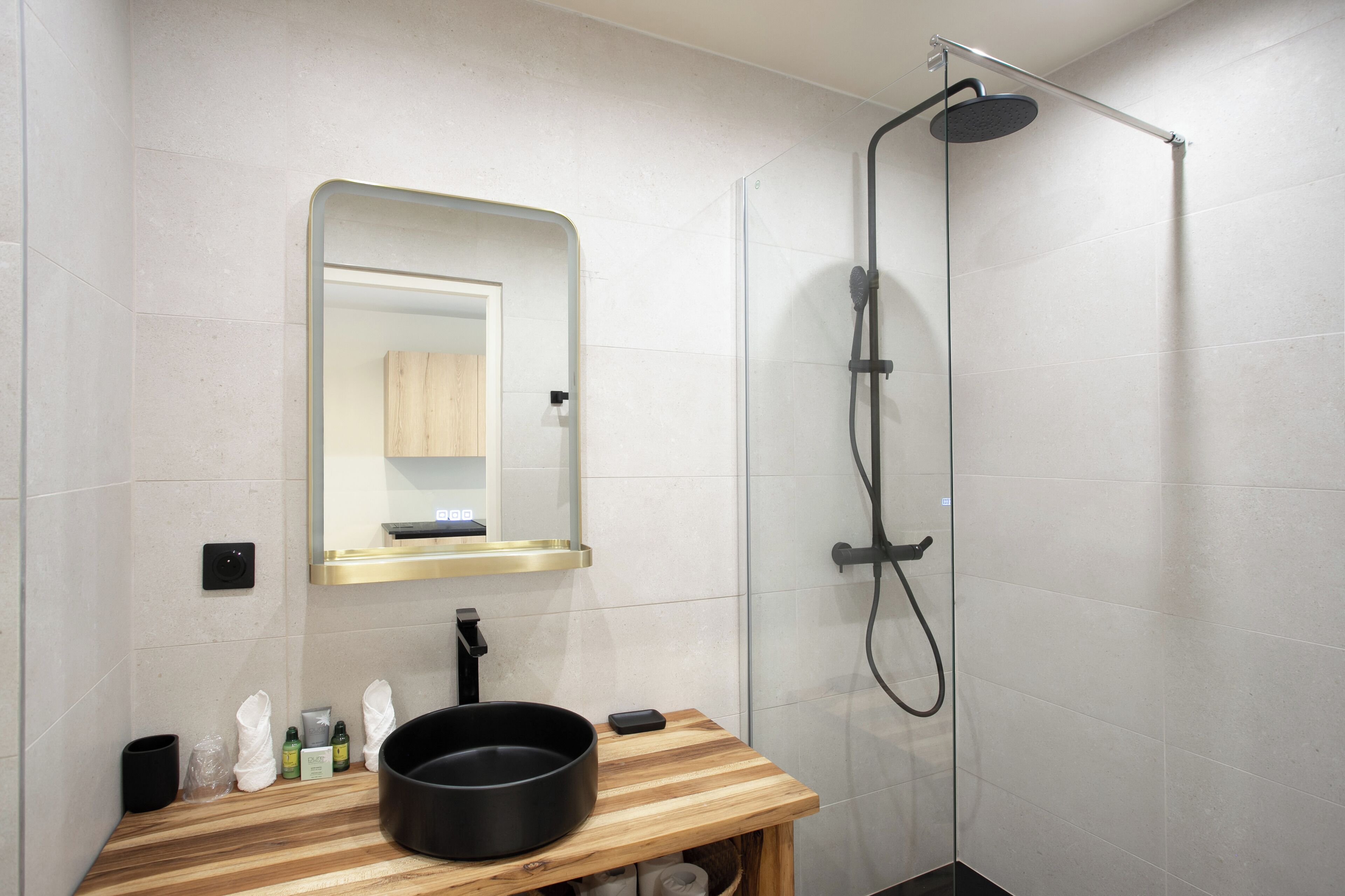 A modern bathroom with a shower, a sink with a black basin, a mirror, and a wooden vanity.
