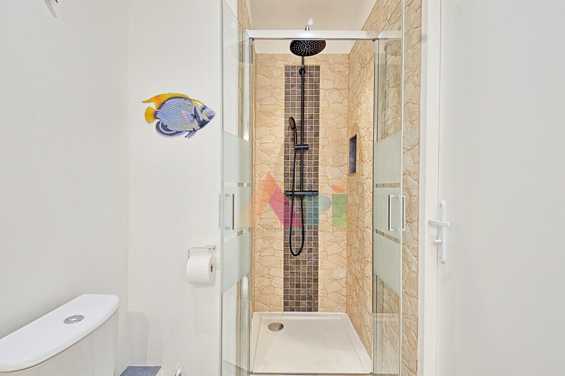 Une douche fermée par des parois en verre, avec un mur carrelé, des toilettes et un porte-serviettes.