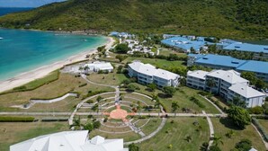 An aerial view of a resort with a beach, a central courtyard, and buildings with blue roofs. - FIDEMAM (Anse Marcel)