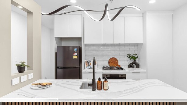 Une cuisine moderne avec des meubles blancs, un plan de travail en marbre, un réfrigérateur en acier inoxydable, une cuisinière à gaz et un luminaire au plafond original.