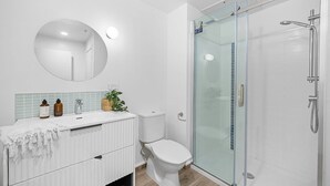 Une salle de bain moderne avec une douche à parois de verre, un miroir rond et un lavabo blanc agrémenté d’articles de toilette.