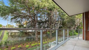 Un balcon doté d’une balustrade en verre, donnant sur un jardin planté d’arbres et d’arbustes.