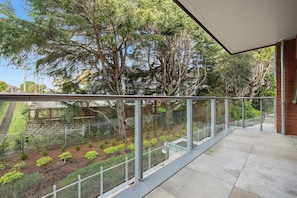 A balcony with a glass railing overlooking a garden with trees and shrubs. - Entire Apartment Near Retails, Green Space & City (Auckland)
