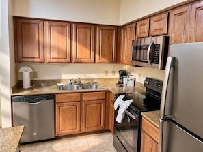A kitchen with wooden cabinets, stainless steel appliances, a dishwasher, and a granite countertop.