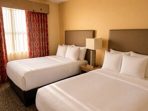 Ein Hotelzimmer mit zwei Betten, einem Nachttisch mit Lampe und einem Fenster mit Vorhängen.