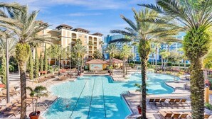 A hotel pool area with palm trees, lounge chairs, and a building in the background. - Apt Resort 3br, Sleeps 10 Disney 10 min (Orlando)