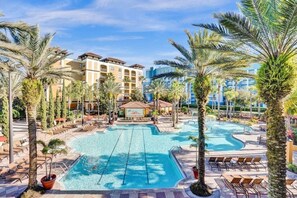 A hotel pool area with palm trees, lounge chairs, and a building in the background. - Apt Resort 3br, Sleeps 10 Disney 10 min (Orlando)