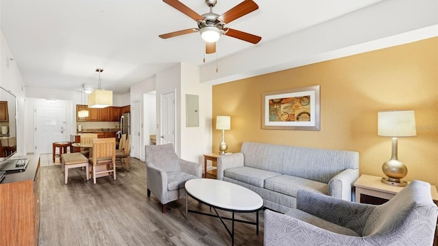 A modern living room with a sofa, chairs, a coffee table, a ceiling fan, and a kitchen in the background. - Apt Resort 3br, Sleeps 10 Disney 10 min (Orlando)