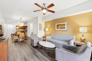 A modern living room with a sofa, chairs, a coffee table, a ceiling fan, and a kitchen in the background. - 3BR Resort Suite on I-drive (Orlando)