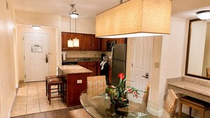 A modern kitchen with wooden cabinets, a central island, a dining area with a glass table, and a large pendant light. - Apt Resort 3br, Sleeps 10 Disney 10 min (Orlando)