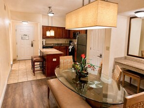 A modern kitchen with wooden cabinets, a central island, a dining area with a glass table, and a large pendant light. - Apt Resort 3br, Sleeps 10 Disney 10 min (Orlando)