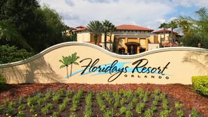 Letrero del resort Floridys en Orlando, con parte superior curva, palmeras y un primer plano con jardines.
