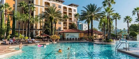 A hotel with a swimming pool, palm trees, and a building with balconies.