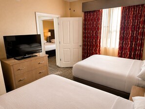 A hotel room with a television on a wooden dresser, a bed with white bedding, a door leading to another room, and red patterned curtains. - 3BR Resort Suite on I-drive (Orlando)