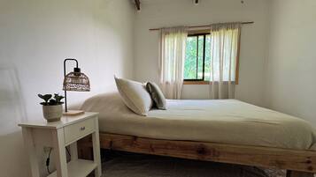 Une chambre à coucher avec un lit en bois, une table de chevet avec une lampe et une fenêtre avec des rideaux.