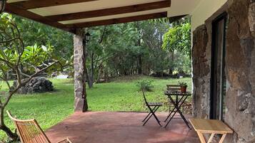 Une terrasse couverte, dotée de chaises et d’une table en osier, de murs en pierre et offrant une vue sur un jardin luxuriant.