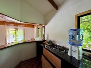 Een keuken met een gasfornuis, een waterdispenser en een raam met uitzicht op groen.