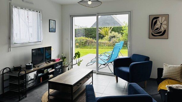 Een moderne woonkamer met een televisie, een salontafel en een bank. Er is een schuifdeur naar een tuin.
