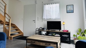 Een moderne woonkamer met een houten trap, een flatscreen televisie, een eettafel en een boekenplank.