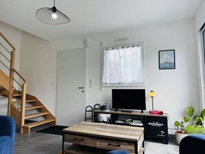 Ein modernes Wohnzimmer mit einer Holztreppe, einem Flachbildfernseher, einem Esstisch und einem Bücherregal.