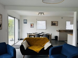 Ein modernes Wohnzimmer mit einer Couch, einem Essbereich mit Tisch und Stühlen, einer Küchenzeile und einem großen Fenster, das für natürliches Licht sorgt.