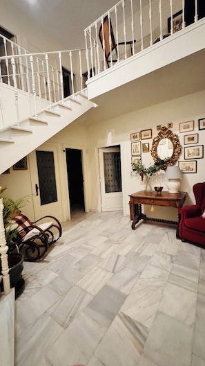 A spacious interior with a white staircase, a red armchair, a wooden table with a vase, and a wall decorated with framed pictures. - Casa Sevilla-Giralda, a villa with a pool just a few minutes from downtown Seville (Mairena del Aljarafe)
