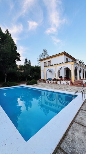 A swimming pool with a white deck, a building with a yellow facade, and arched windows. - Casa Sevilla-Giralda, a villa with a pool just a few minutes from downtown Seville (Mairena del Aljarafe)