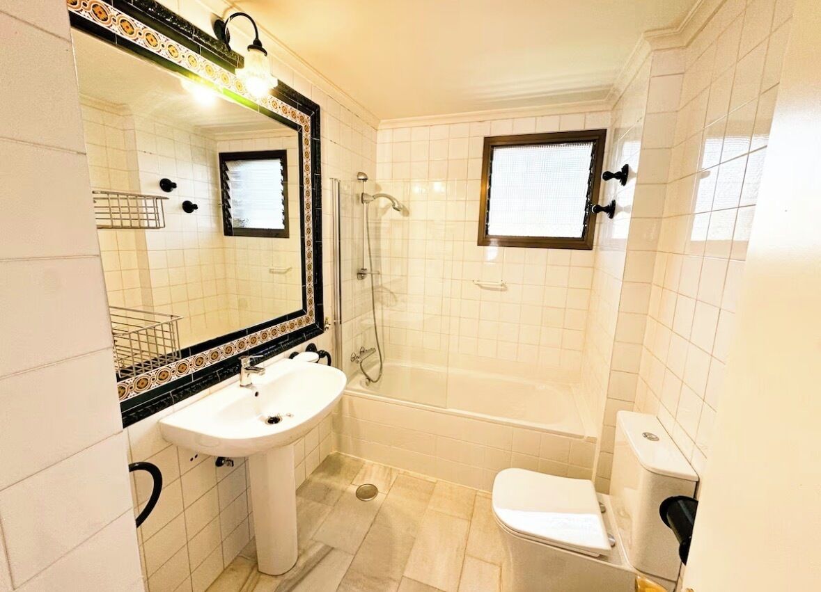 A bathroom with a white sink, a mirror with a decorative frame, a bathtub, and a toilet.