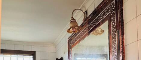 A bathroom with a white sink, a mirror with an ornate frame, and a window with a grid pattern.