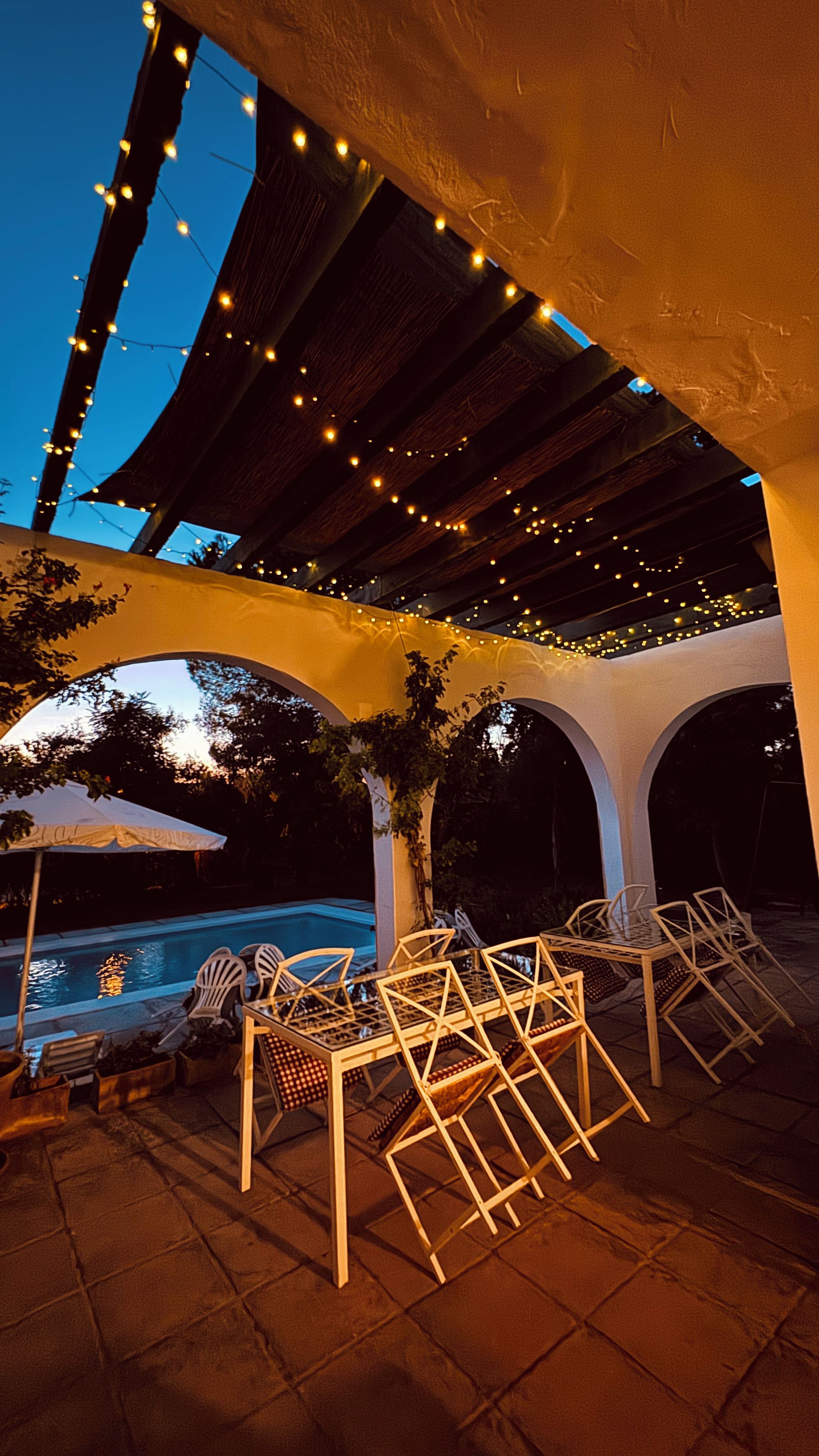 An outdoor patio area with a pool, chairs, and string lights.