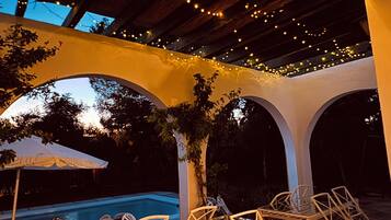 An outdoor patio area with a pool, chairs, and string lights.