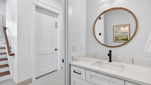 Un baño con tocador blanco, un espejo redondo y una puerta que da a otra habitación.