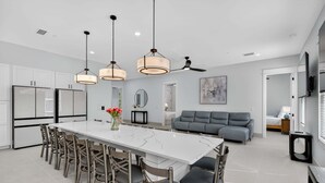 Una cocina moderna con una isla de mármol, luces colgantes y un comedor con sillas.