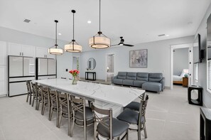A modern kitchen with a marble island, pendant lights, and a dining area with chairs. - Golden Getaway — Luxury Coastal Home Near Beach (Santa Rosa Beach)