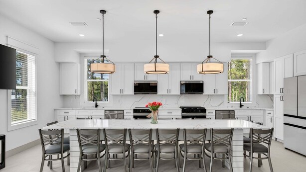Una cocina moderna con armarios blancos, una isla grande con asientos, iluminación colgante y un televisor de pantalla plana.