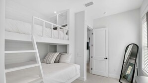 Una habitación blanca con literas, una puerta y un espejo.