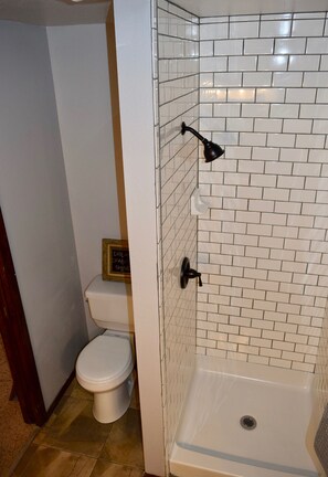 A bathroom with a white toilet, a shower with white tiles, and a small framed sign on the wall. - Triple L Ranch. Working Cattle Ranch. Dog Friendly. 10 minutes to Snake River. (Huntington)