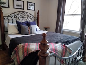 A neatly made bed with a headboard, a bedside table, and a window with curtains. - Triple L Ranch. Working Cattle Ranch. Dog Friendly. 10 minutes to Snake River. (Huntington)