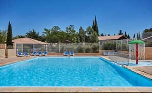 Une piscine rectangulaire à l’eau d’un bleu limpide, entourée d’une basse clôture. Plusieurs chaises longues bleues sont alignées le long du bord de la piscine.
