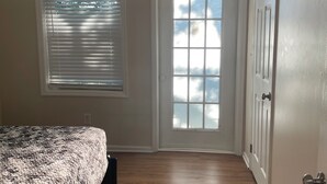Um quarto com cama, porta e janela com persianas.