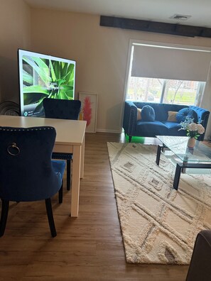 A living room with a blue sofa, a glass coffee table, a white table, and a blue chair.