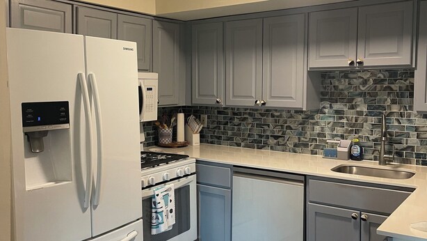 Uma cozinha moderna com armários cinza, uma geladeira branca, um fogão e um painel de azulejos.